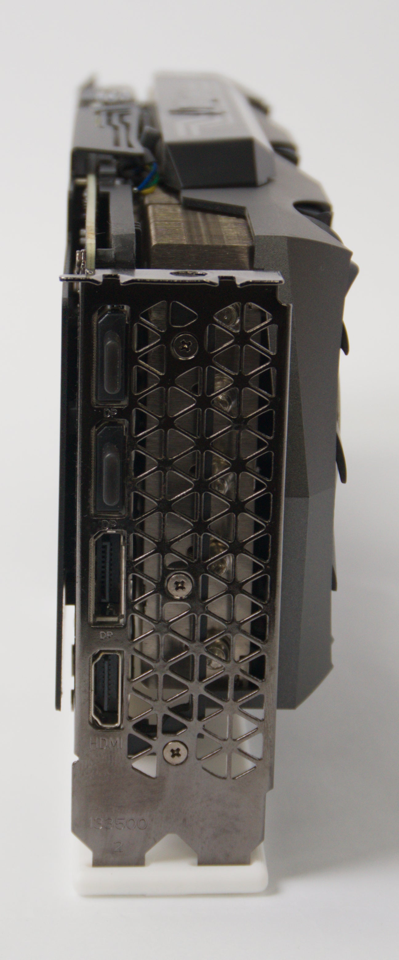 Close-up of the rear or side I/O area of a black graphics card with a honeycomb-patterned metal shroud and visible ports, photographed on a light gray background.