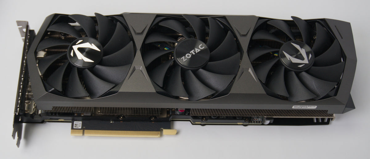 A Zotac three-fan graphics card with a black and dark gray triple-shroud cooling system, shown from a high angle on a light gray background.